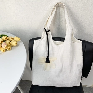 Detailed close-up of white pleated canvas tote bag with floral charm on a chair