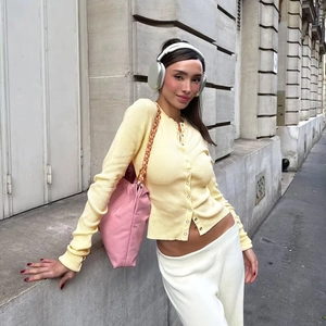 Dettaglio del cardigan in maglia gialla con bottoni metallici e vestibilità aderente