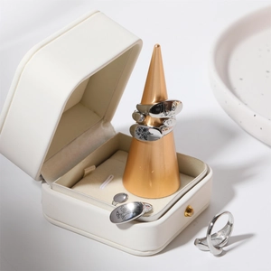 Silver flower engraved ring set on a gold display stand with a white jewelry box