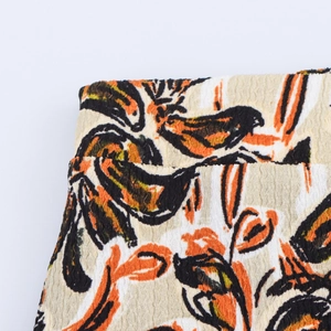 Detail aus plissiertem Stoff mit orangefarbenem und schwarzem botanischem Blumenmuster