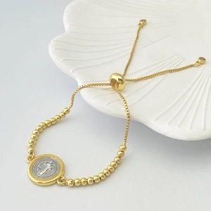 Detail of two-tone Saint Benedict heart charm bracelet with adjustable beaded closure