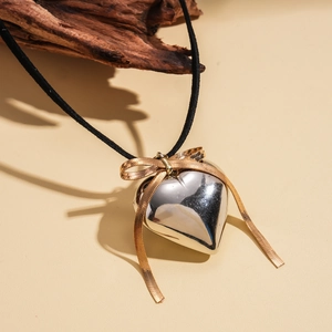 Detail of silver heart pendant with gold bow on black cord over neutral background