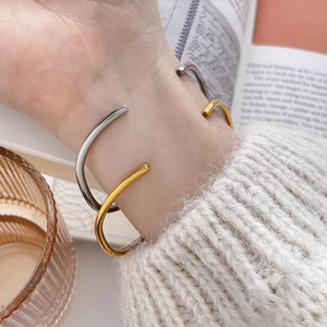 Close-up of gold and silver minimalist open C-shaped bracelets on a wrist with a sweater