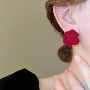 Elegant model wearing deep red flocked camellia flower stud earrings with a matte texture