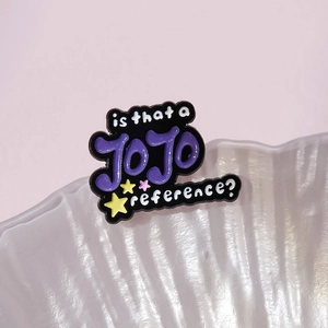 Detail of enamel JOJO reference pin featuring colorful letters on a white shell plate
