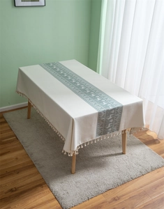 Detail of cream jacquard tablecloth featuring teal Nordic reindeer patterns and fringe edge