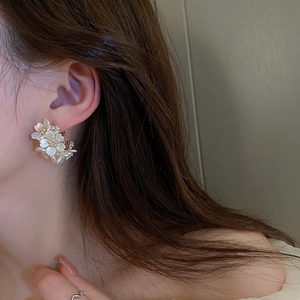 Elegant white floral shell stud earring displayed on a model's ear in close-up detail