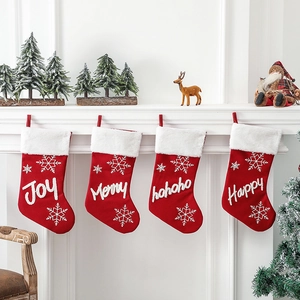 Four red plush Christmas stockings with white embroidery hanging on a fireplace