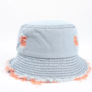 Dettaglio di un cappello a secchiello in denim blu con fori arancioni e bordi sfrangiati