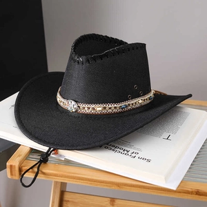 Black straw cowboy hat with ethnic shell band and chin strap on a modern book