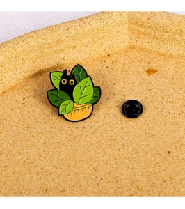 Detailed view of cute black cat enamel pin hiding behind a green potted plant