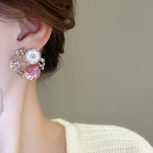 Detail of floral earrings with pink resin petals and crystal accents on a model