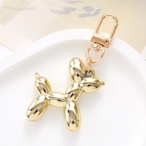 Macro shot of a glossy gold balloon dog keychain with a metallic lobster clasp on a white tray