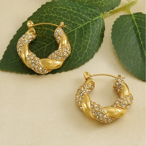 Close-up of gold twist hoop earrings with pavé crystals on a textured fabric background