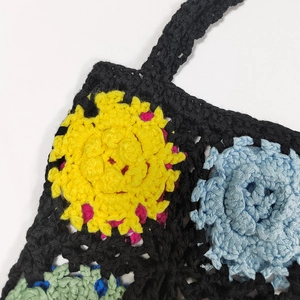Close-up of handmade crochet flower patterns on the black woven tote bag details