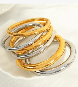 Detailed close-up of polished 18K gold and silver bangles on white ceramic display