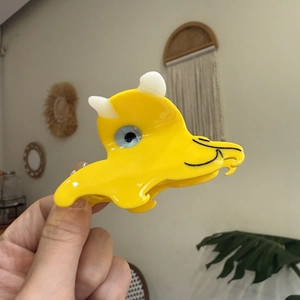 Cute yellow dinosaur hair claw clip made of acetate resin shown in a natural indoor setting