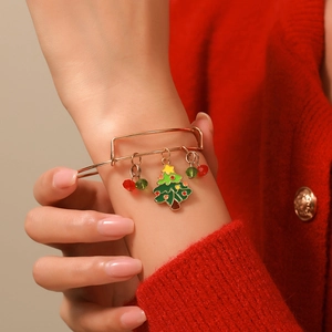 Close-up of adjustable Christmas tree bangle with green and red charms on female model