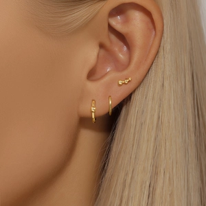Detailed view of three minimalist gold hoop earrings and stud set worn on ear