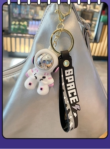 Detailed view of white astronaut keychain with pink accents and black SPACE wrist strap