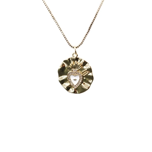 Macro detail of a gold-plated sacred heart pendant with white enamel and micro-crystals