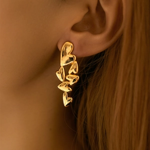 Close-up of model wearing gold heart earrings with irregular liquid metal texture