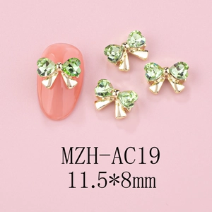 Macro detail of gold bow nail charms with green rhinestones sized 11.5x8mm on pink base