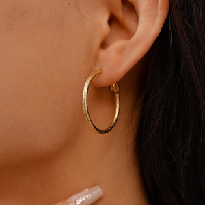 Detail of golden textured matte hoop earring shown on ear for fashionable daily wear