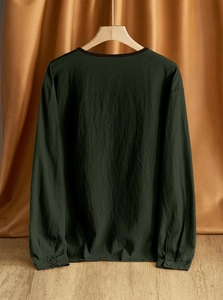 Detail of the back of a dark green linen shirt featuring buttoned cuffs on a wooden hanger