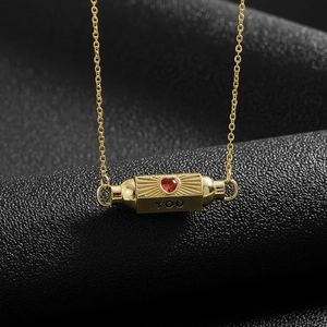 Macro shot of gold cylindrical pendant with red heart gemstone and 'YOU' engraving