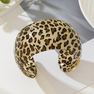 Macro detail of the wide C-shaped leopard print resin bangle on a clean minimalist surface