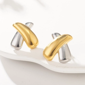 Detail of high-polished gold and silver overlapping X-shape stud earrings on white pedestal