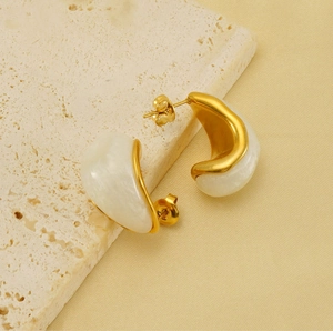 Detail of vintage gold-plated teardrop earrings on textured stone with pearly white resin