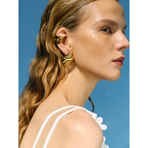 Golden conch shell earrings and C-shaped ear cuff shown on a model against blue sky
