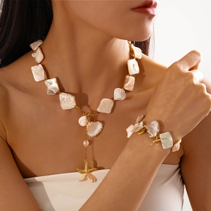 Detailed shot of starfish and shell charms on a gold seaside necklace with baroque pearls