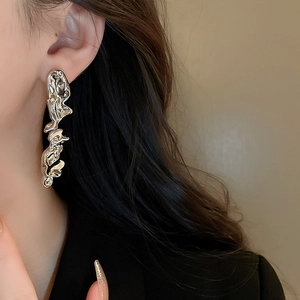 Detail view of silver irregular liquid metal earrings worn by a model on plain background