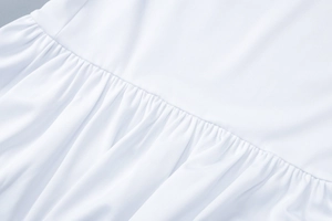 Nahaufnahme der weißen Stofftextur mit detaillierten Raffungen und feinen Nähten am Kleid