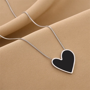 Minimalist silver snake chain necklace with a black heart pendant on draped fabric