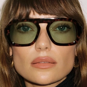 Close-up of oversized tortoise frame sunglasses with green lenses on model face