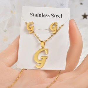 Dettaglio del set collana e orecchini in acciaio dorato con ciondolo a forma di lettera G