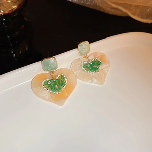 Détail de la boucle d'oreille cœur marbré crème avec pierres vertes et dorées