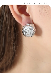 Macro shot of silver stud earrings featuring a modern hammered metal finish on model