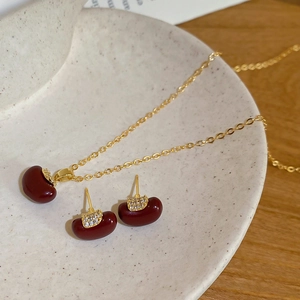 Detailed close-up of gold-plated apple pendant and earrings set on a beige plate