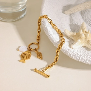 Detail of gold titanium steel bracelet featuring sea shell and fishbone charms with toggle clasp