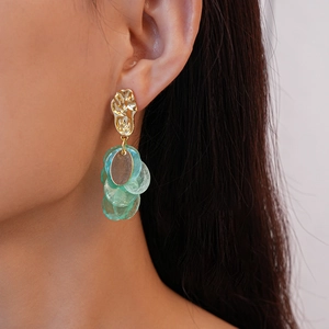 Close-up of model wearing gold irregular earrings with green translucent pendant charms