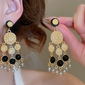 Détail des boucles d'oreilles bohèmes dorées avec perles noires et pompons gris