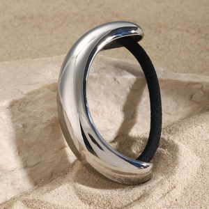 Sleek silver stainless steel ponytail holder on a natural rock with a sandy background