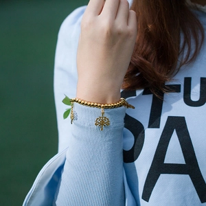 Bracelet à perles dorées avec pendentifs arbre de vie, porté par un mannequin en extérieur
