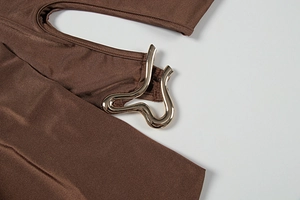 Détail d'une robe marron foncé avec une boucle métallique dorée ondulée sur l'épaule