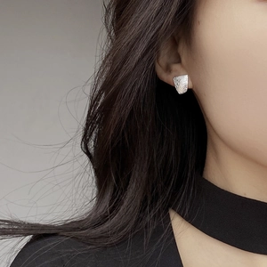 Irregular geometric silver stud earrings with hammered texture on female model ear